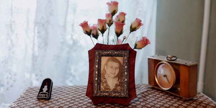 Framed vintage portrait of a young girl on a table with pinkish roses behind it and a small memorial candle and clock nearby.