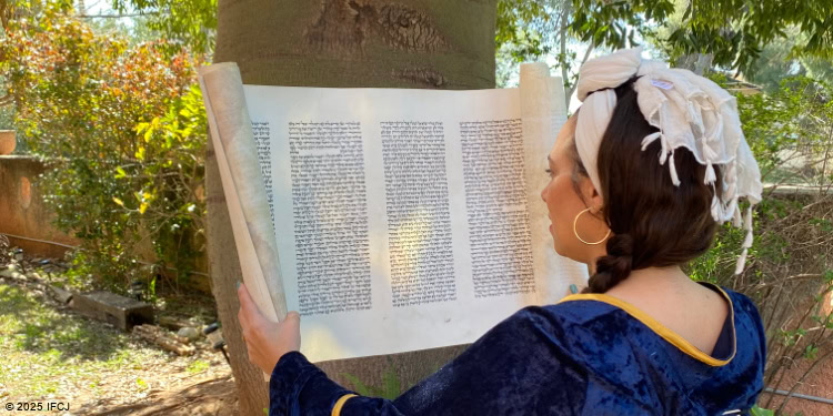 Jewish woman reading Torah outdoors under a tree, engaging with sacred text in a peaceful garden setting.