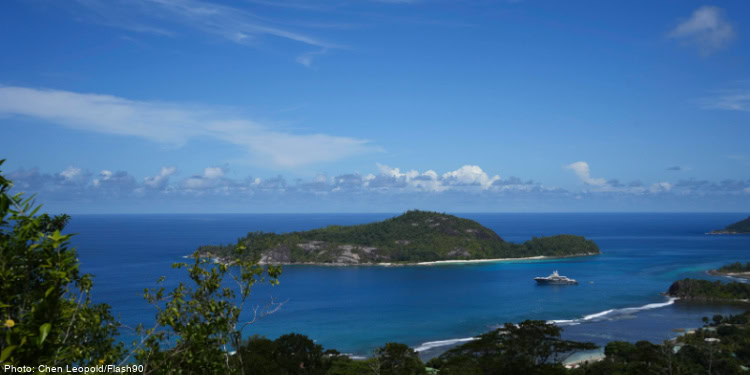 Beautiful tropical island surrounded by vibrant blue ocean and clear skies, featuring lush green foliage and a cruise ship docked nearby, showcasing a serene and picturesque coastal landscape.