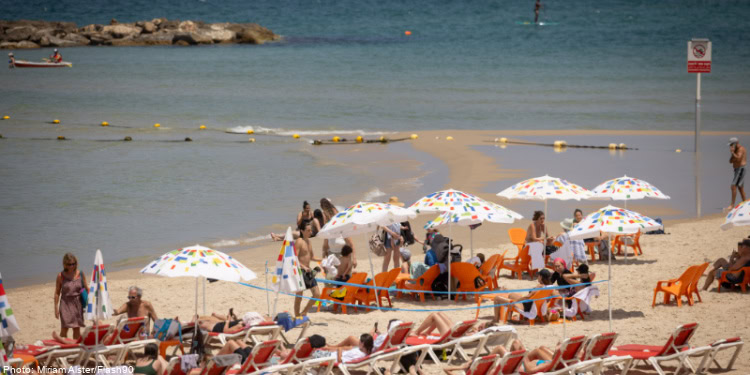 Beach scene with umbrellas, sunbathers, and families enjoying a sunny day at the seaside.