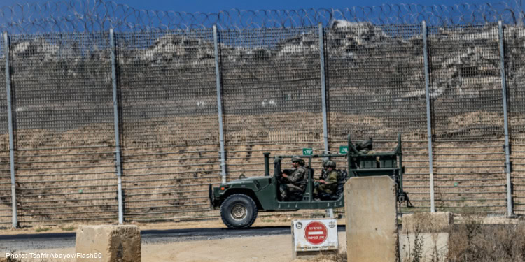 Military vehicle patrolling near a security fence at a border area.