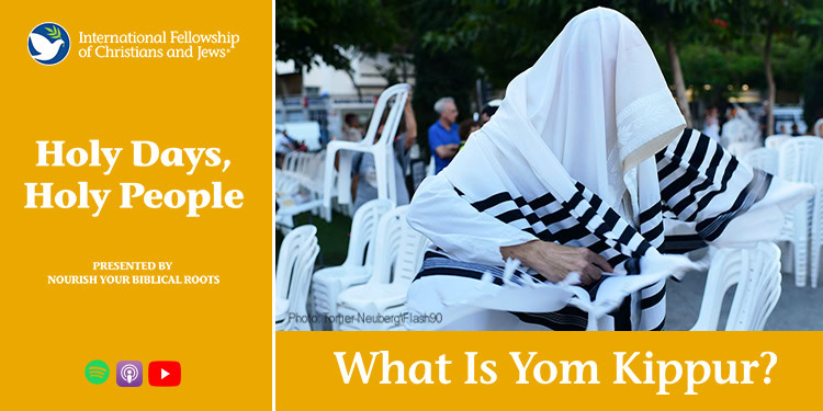 Person wearing tallit praying outdoors during Yom Kippur, with chairs and trees in the background, symbolizing Jewish tradition and reflection.