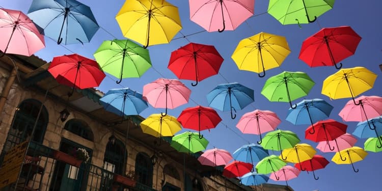 Several umbrellas hanging from a laundry line overhead a street in Jerusalem.