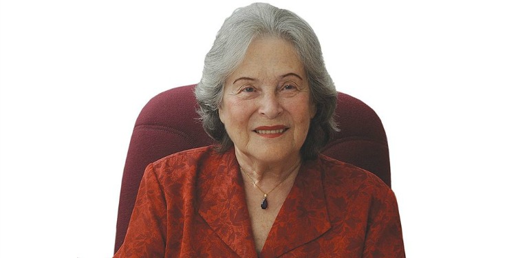 Elderly woman sitting in a red chair smiling at the camera.