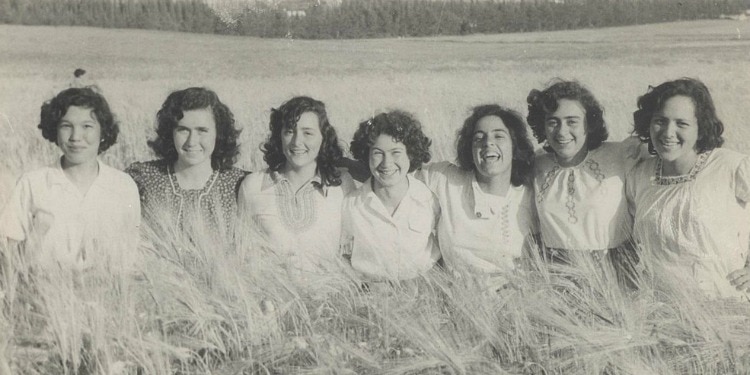 Black and white photo of seven women standing together in a wheat field.