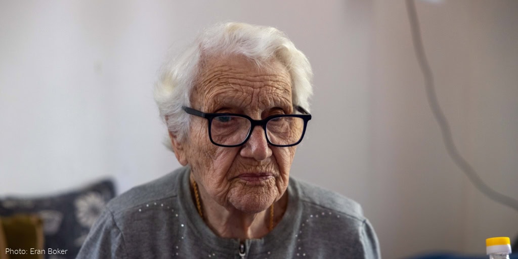 Elderly woman, gray sweater, glasses - somber expression