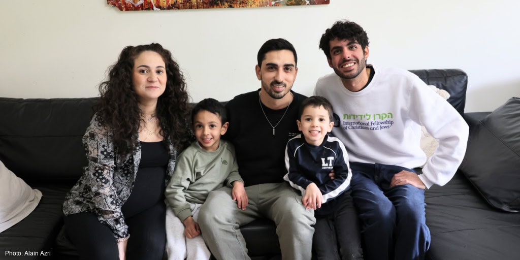 A diverse Jewish family sitting together on a sofa, smiling and enjoying quality time, symbolizing hope, unity, and support for Jewish families through IFCJ programs.