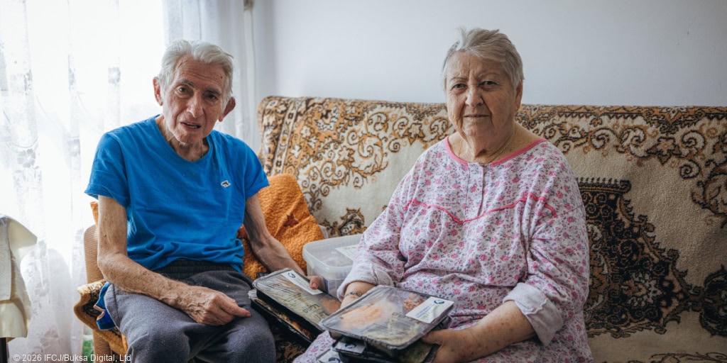 Elderly man and woman sitting on a sofa, reading books and sharing a moment of companionship, symbolizing hope and support for vulnerable seniors through IFCJ's Shine a Light initiative.