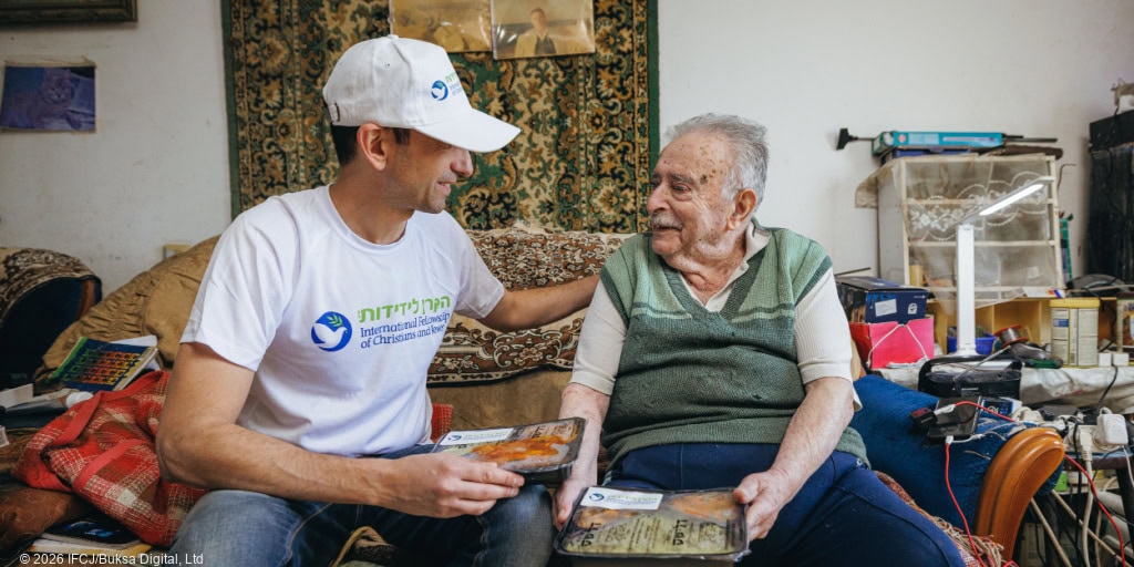 Volunteer sharing a meal with elderly woman in a cozy home setting, symbolizing compassion and support for vulnerable communities.