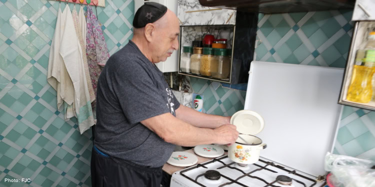 FJC Coronavirus Emergency Assistance Food Deliveries, elderly man standing at stove stirring pot, gray shirt, black pants, yarmulke