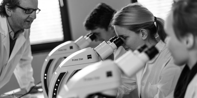 Black and white photo of three students looking through a microscope.