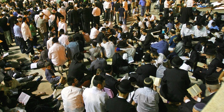 Group of men gathered together sitting down on the floor and reading scripture.