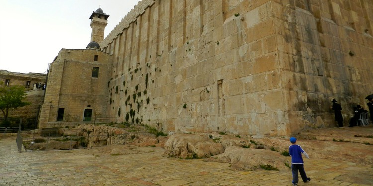 A young boy in blue walking towards an old building.