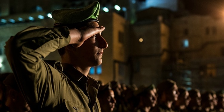 Group of IDF soldiers saluting outside of a building late at night.