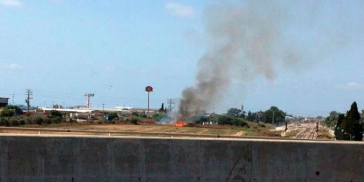 Smoke rising into the air from a rocket strike near a highway.