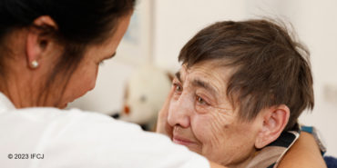 Elderly Jewish woman smiling up at an IFCJ staff member.