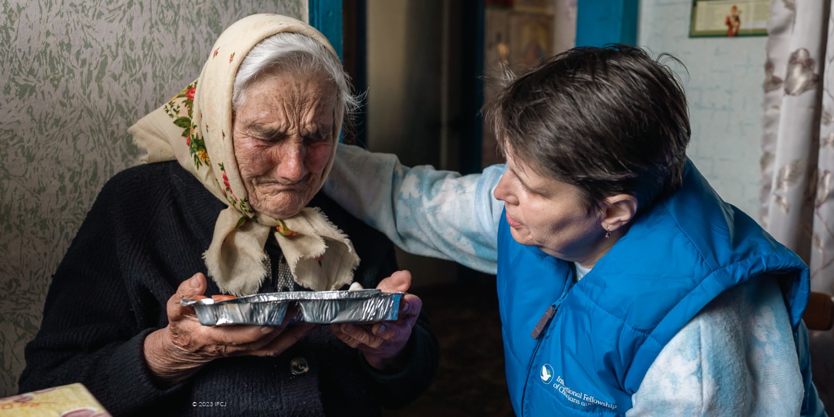 Elderly Jewish woman crying over a donated hot plate as she sits with an IFCJ volunteer.