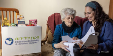 Yael Eckstein sitting next to an elderly Jewish woman with an IFCJ branded food box.