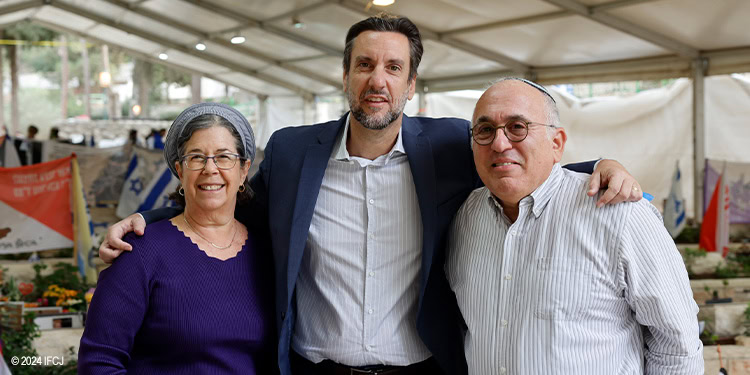 Friendly group of three people smiling and embracing at an IFCJ charity event, showcasing community, support, and humanitarian aid efforts.