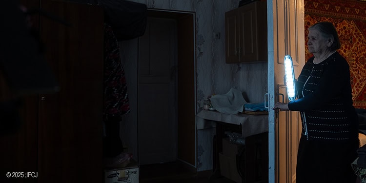 Elderly woman walking through a dark doorway holding an electric lamp