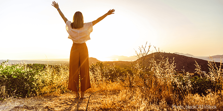 A woman standing outdoors with arms raised in celebration during sunset, symbolizing joy and gratitude. The scene reflects hope, faith, and the blessings of life, aligning with themes of spiritual rej.