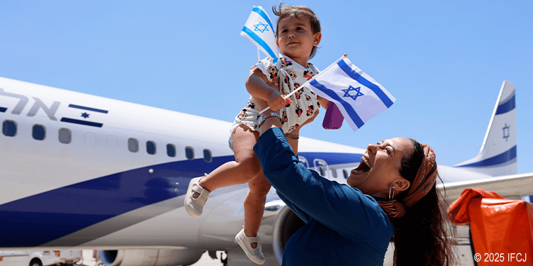 Yael holding a baby in the air with a plane in the background