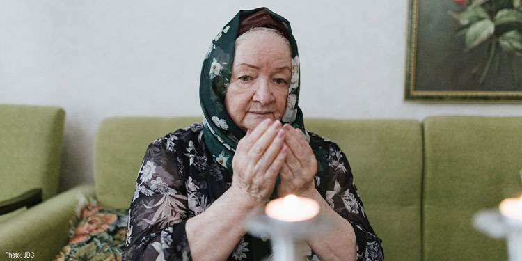 Elderly woman sitting on a green couch praying
