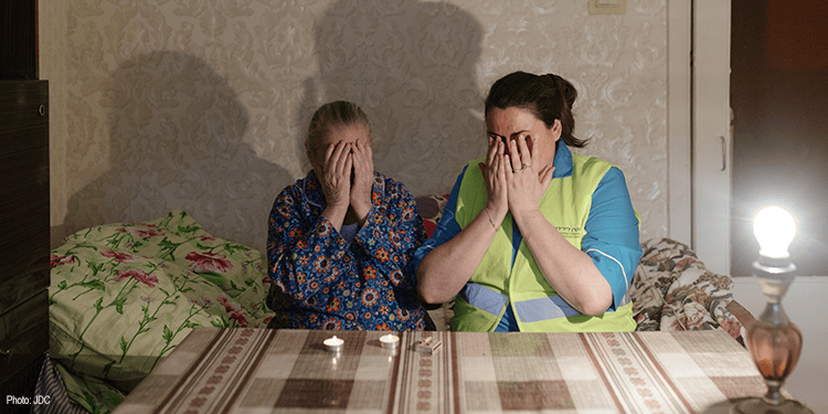 Elderly woman and IFCJ volunteer holding their hands over their eyes praying