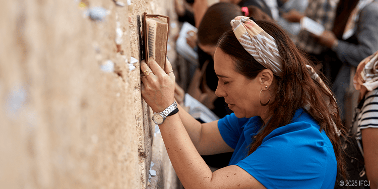 Woman praying at the Western Wall in Jerusalem, a sacred site for Jewish worship and reflection, with a group of people engaged in prayer and spiritual connection.