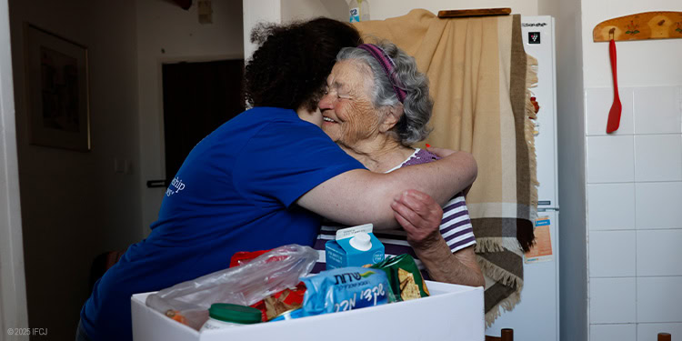 IFCJ Staff hugging an elderly woman holding a food box