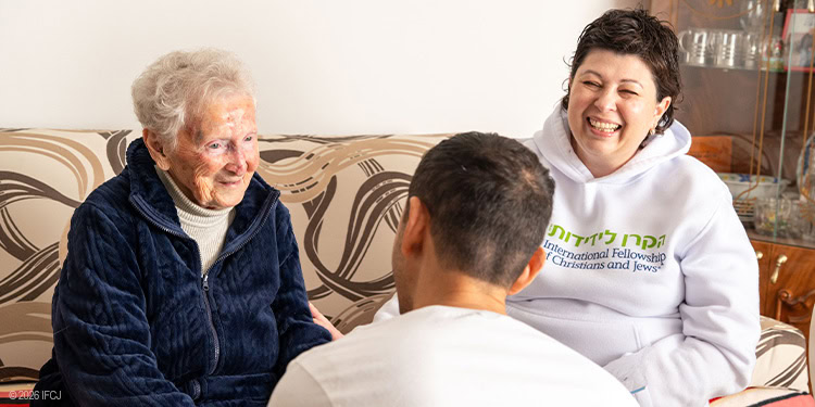 IFCJ Staff and elderly woman sitting on the couch smiling