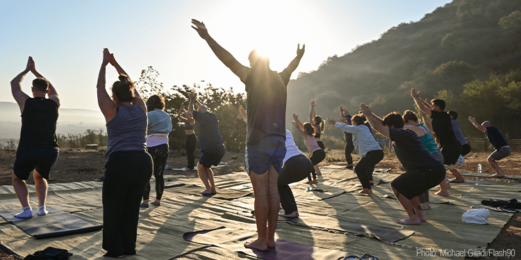 Yoga class outdoors at sunrise with participants practicing poses on mats.