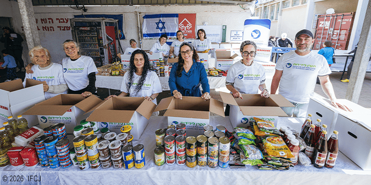 Yael standing with IFCJ volunteers packing food boxes for Passover