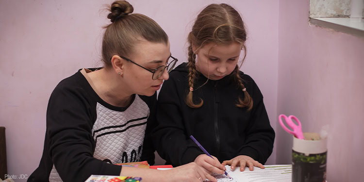 Two young girls studying and writing in a classroom setting, demonstrating focus and collaboration.