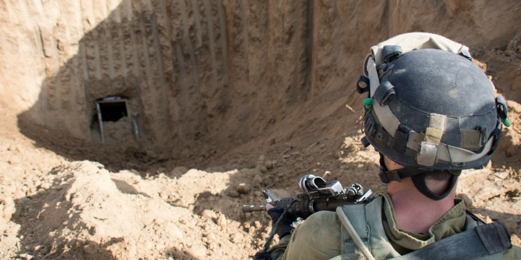 The back of a soldier's head while he's looking down a sandy hole.