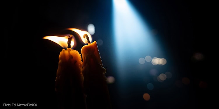 The image features a single lit candle with a glowing flame against a dark background, symbolizing hope, faith, and the pursuit of peace. The soft light highlights the candle's wax and creates a warm, inspiring atmosphere, representing the mission of IFCJ to bring hope and support to those in need