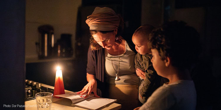 The image depicts a caring woman reading a book to two children in a cozy, softly lit environment, highlighting IFCJ's mission to bring hope, support, and compassion to those in need. The scene emphasizes the importance of community, education, and emotional connection fostered through IFCJ's humanitarian efforts.