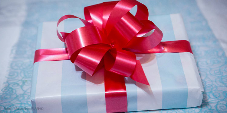 Gift box with red ribbon and bow, symbolizing charity and giving, on a light blue surface. Perfect for representing donations, support, and humanitarian aid from IFCJ.