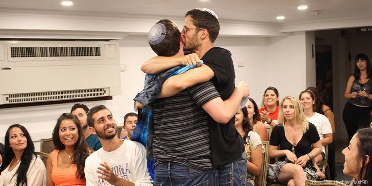 A heartfelt moment of support as a man embraces a young boy, surrounded by an engaged and diverse audience at an IFCJ community event.