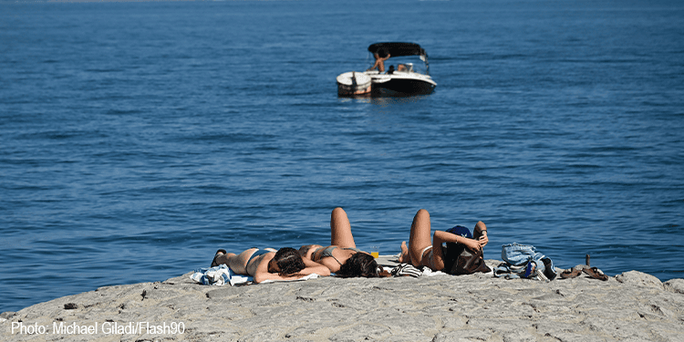 People sunbathing and relaxing on the sandy beach with a boat floating in the water in the background.