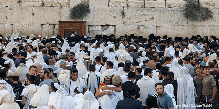 Large gathering of Jewish mourners praying and mourning at the Western Wall, with many wearing traditional white garments and prayer shawls.