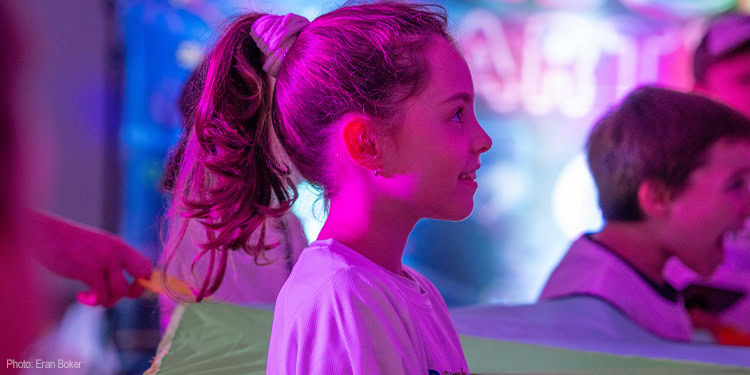 Young girl with a ponytail smiling at a Hope event, surrounded by children in a colorful, vibrant setting, symbolizing hope and community support.