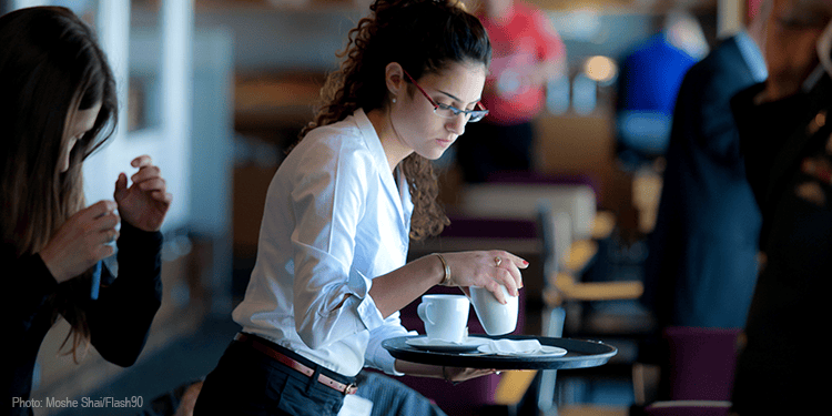 Young woman serving coffee at a restaurant, with other diners in the background, capturing a moment of hospitality and service.
