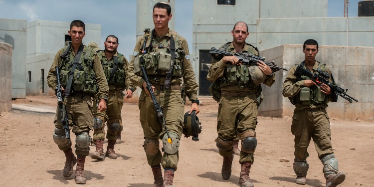 Five IDF soldiers walking outside of a building fully armed.