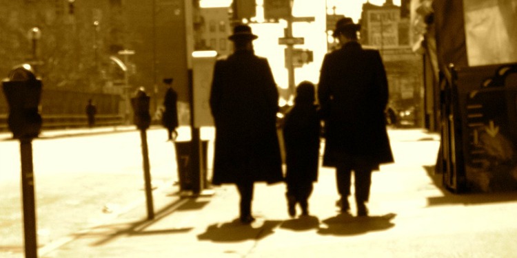 A faded photo from the past of two Orthodox Jewish men walking down the sidewalk with a child