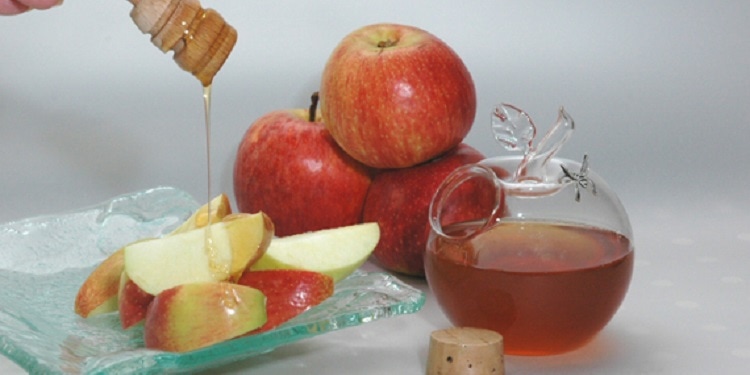 Three apples and cut up apples on a plate with honey beside them.