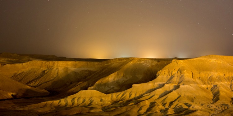 Sandy hills against a lit up nighttime sky.