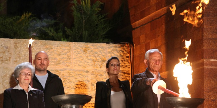 A man using a fire on a black pedestal to light a candle with three people behind him.