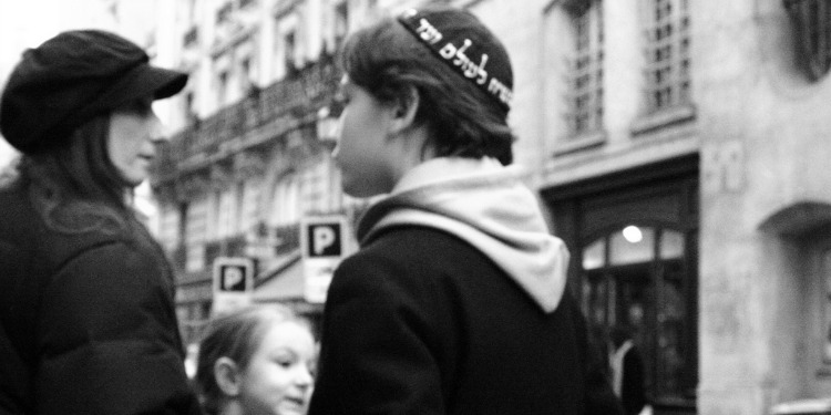 A young boy with a kippah on walking towards his mother and sister.