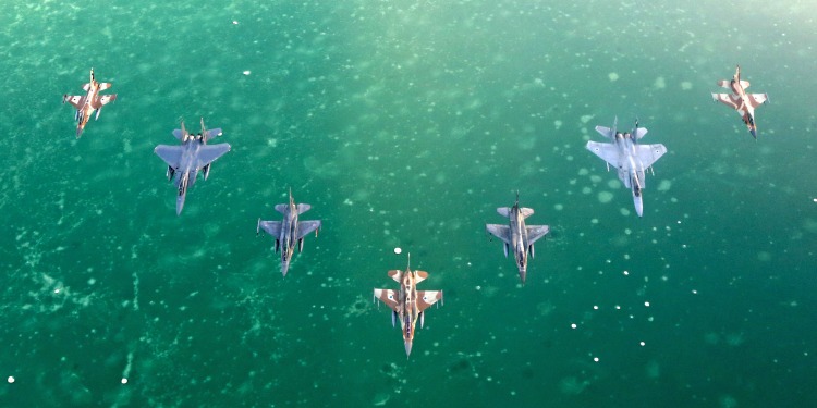 Aerial view of seven fighter jets flying over the ocean.